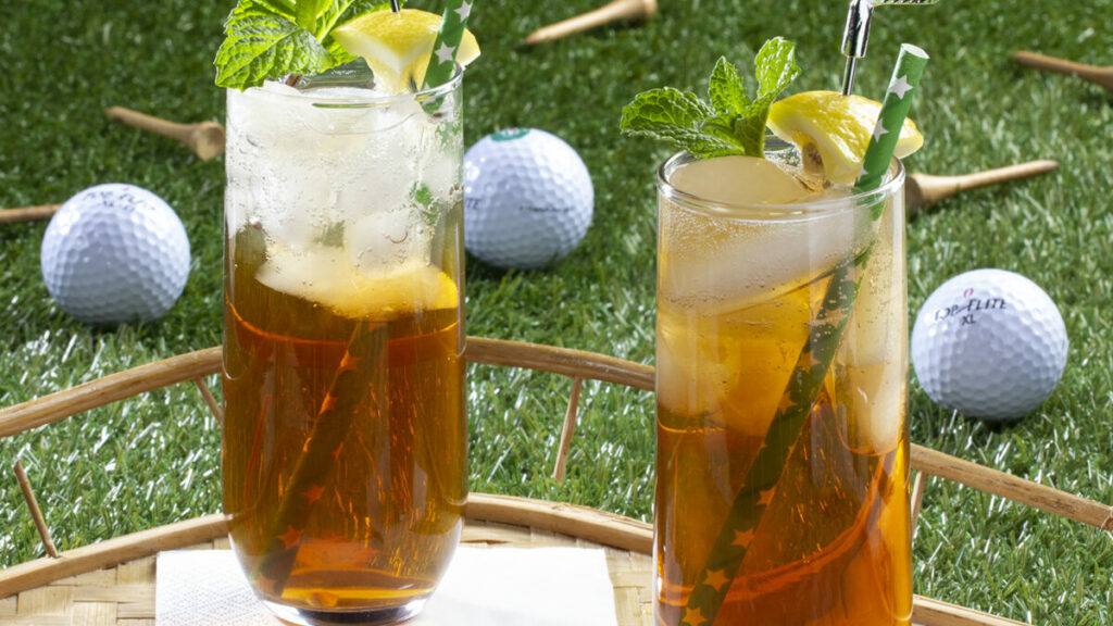 Two glasses filled with an iced tea beverage topped with a mint leaf, and a lemon speared with a mini golf club 