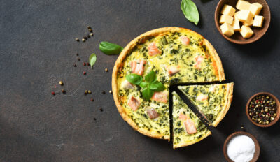 Quiche (pie) with salmon, spinach and soft cheese on a dark concrete background. View from above.