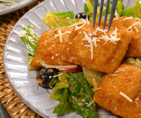 A white plate with fried raviolis on top of a bed of lettuce