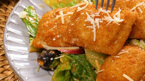 A white plate with fried raviolis on top of a bed of lettuce