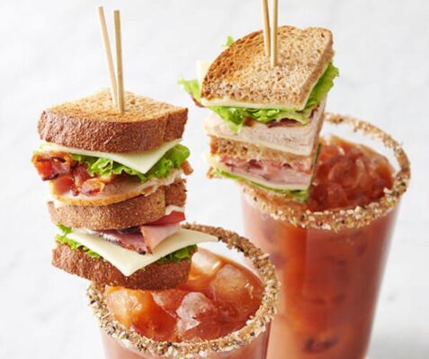 Two glasses of bloody mary cocktails with sandwiches skewerd on top