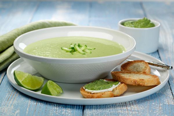 bowl of green soup on a plate with crackers and limes