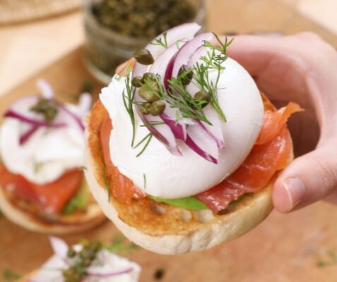 A hand holding an avocado and smoked salmon English muffin