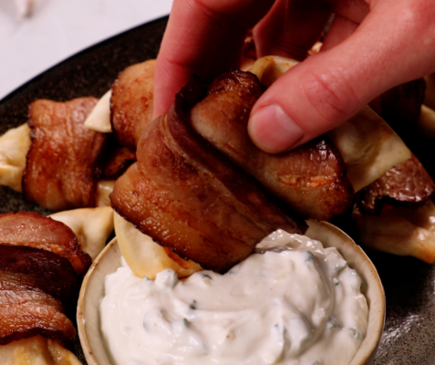 Bacon-wrapped pierogies being dipped into a white sauce