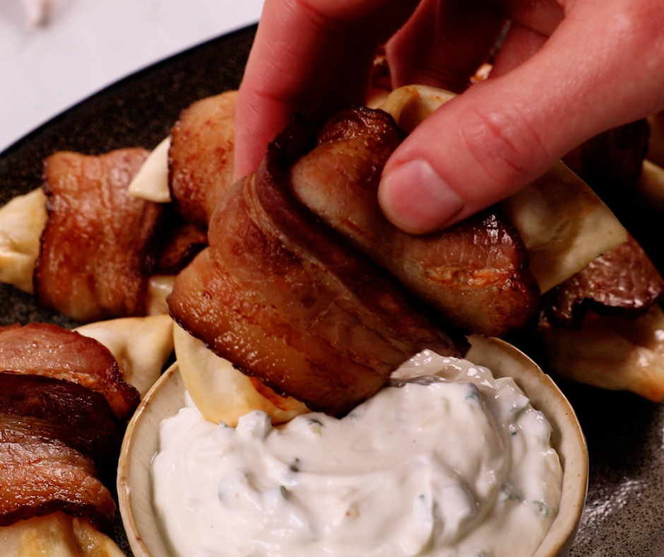 Bacon-wrapped pierogies being dipped into a white sauce