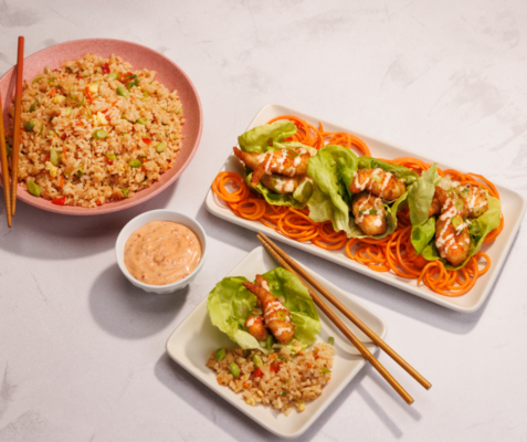 2 square plates with bang bang shrimp lettuce cups next to a bowl of fried rice and a small cup of orange sauce