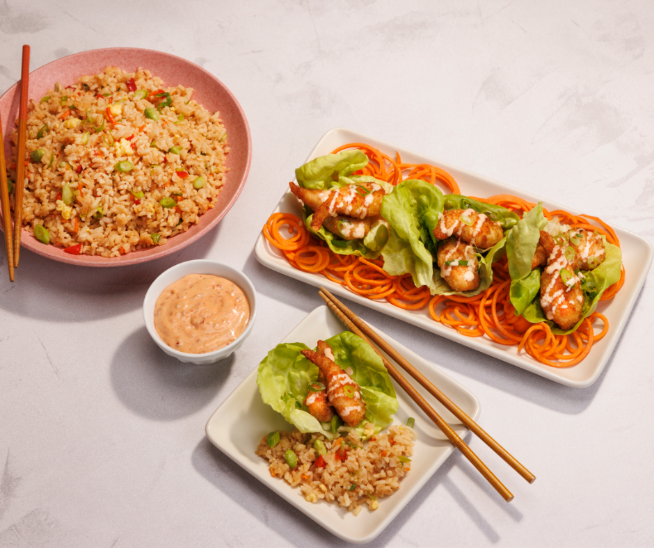 2 square plates with bang bang shrimp lettuce cups next to a bowl of fried rice and a small cup of orange sauce