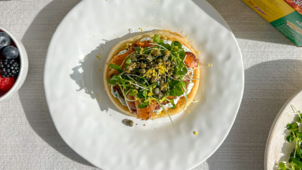 a waffle topped with smoked salmon, cream cheese, and various greens on a plate