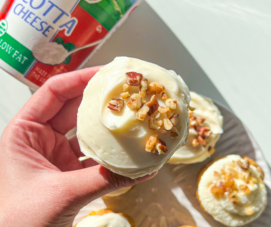 a hand holding a carrot cupcake with ricotta frosting