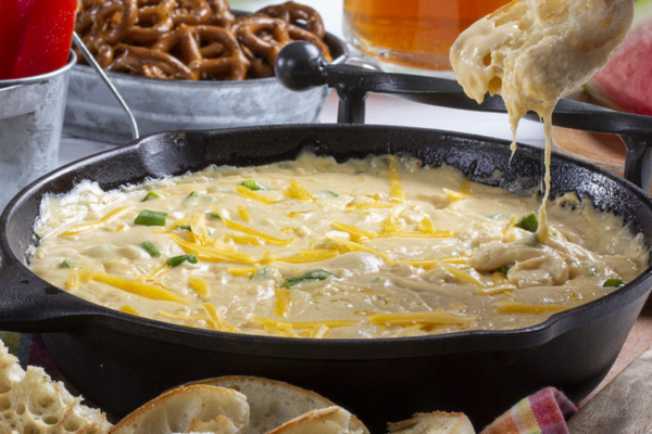 A piece of bread dipping into a skillet of cheesy beer dip