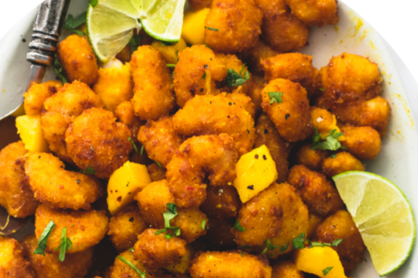 close up shot of popcorn shrimp with seasonings and limes