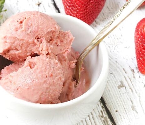 Close up shot of a strawberry frozen yogurt in a white bowl being scooped with a silver spoon
