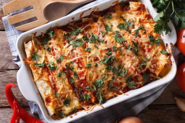 Overhead shot of Chicken and Cheese Enchiladas in a white pan next to a wooden fork and spoon