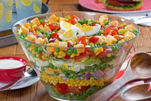 Close up image of a large glass bowl filled with layers of veggies and eggs