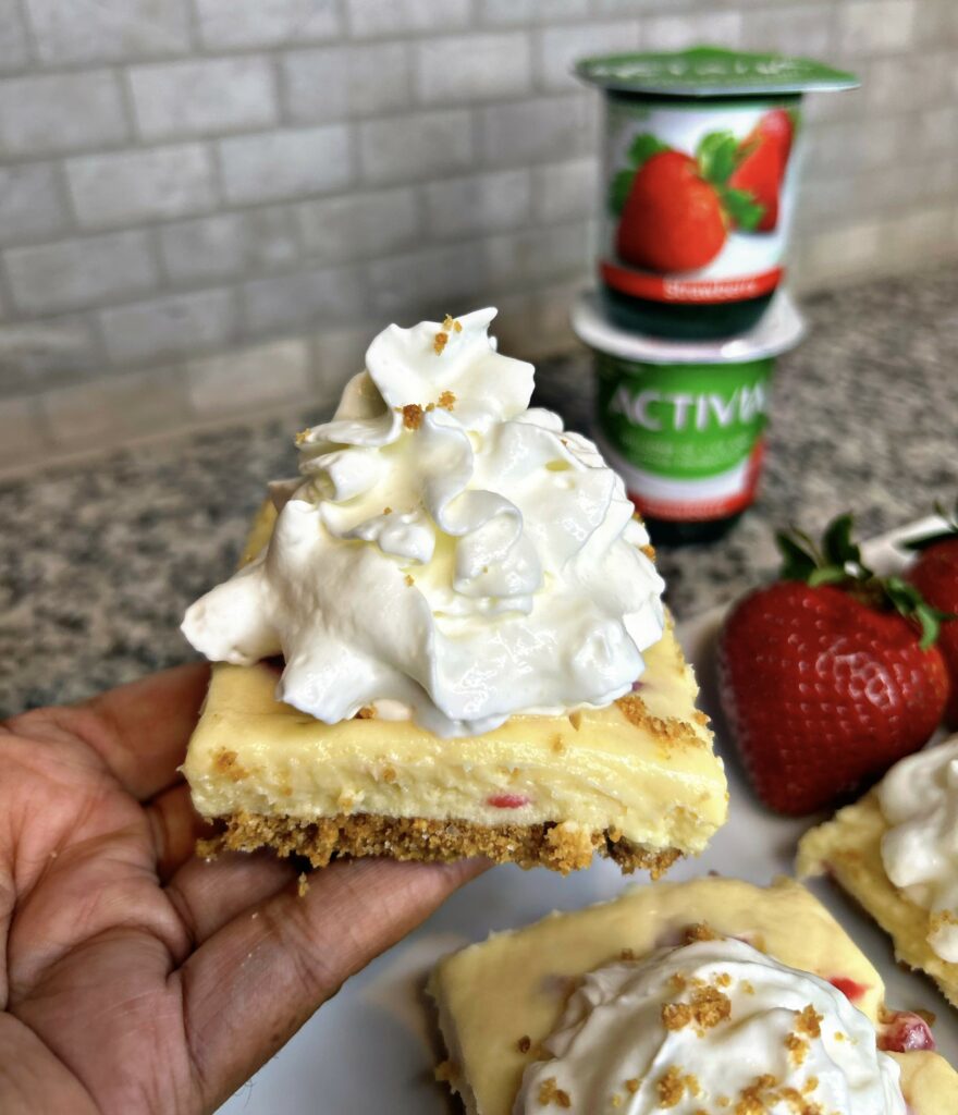 a hand holding a dessert bar with whipped cream on top