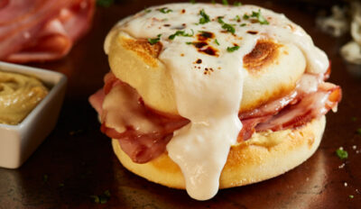 Zoom in on English muffin with ham and cheese toasted and drizzled with a white sauce sprinkled with herbs