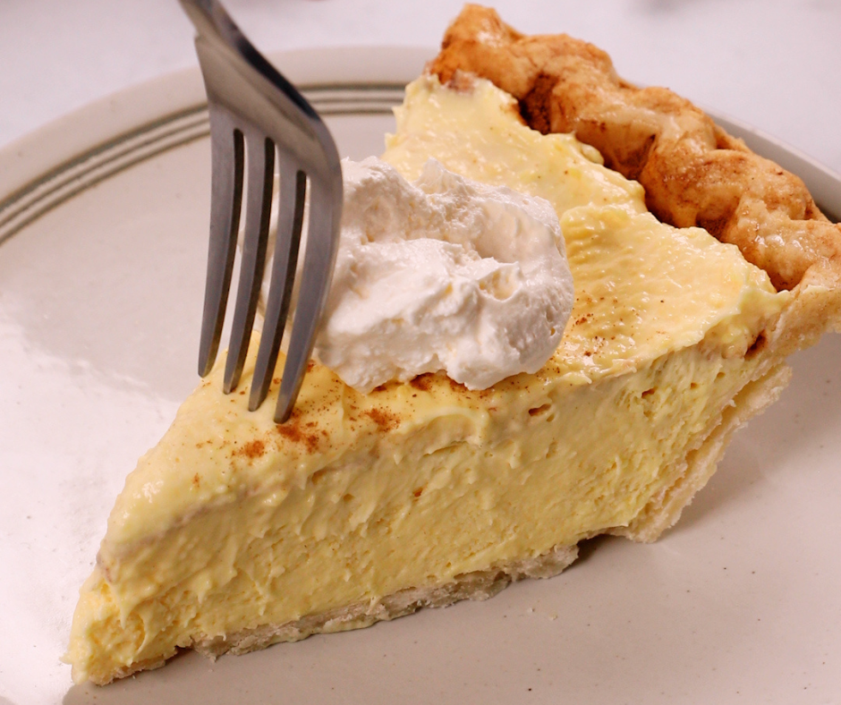 A fork going into a slice of eggnog pie topped with whipped cream