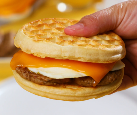 A hand holding a waffle breakfast sandwich