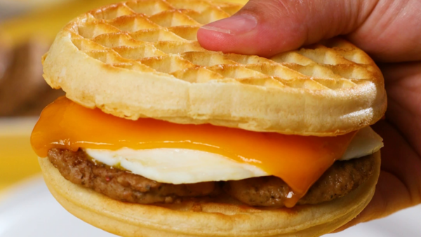 A hand holding a waffle breakfast sandwich