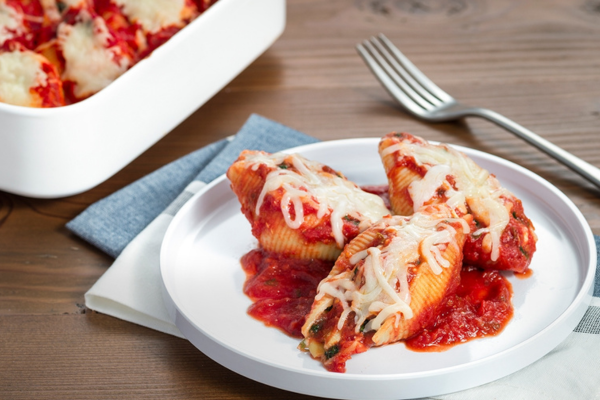 Close up shot of eight cheese stuffed shells on a white plate and a silver fork behind it