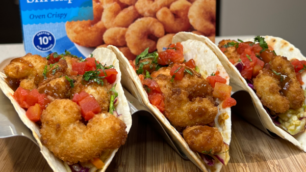 Close up of 3 fish tacos side by side and a box of seapak frozen popcorn shrimp in the background