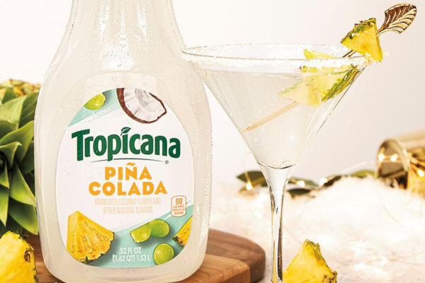 A bottle of tropicana pina colada juice sitting next to a martini glass filled with a frosted coconut martini drink
