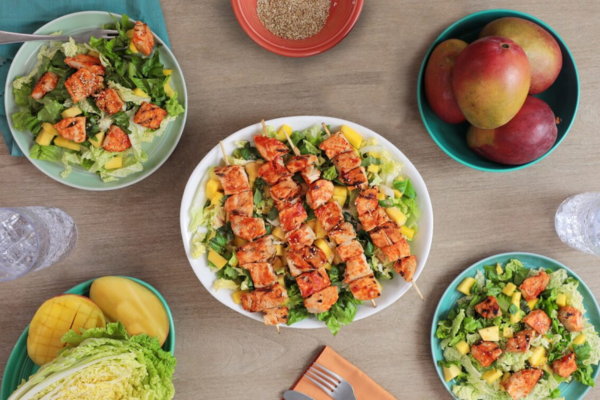 Close up shot on a White Bowl Filled with salad topped with chicken and surrounded by 5 bowls filled with various salad ingredients