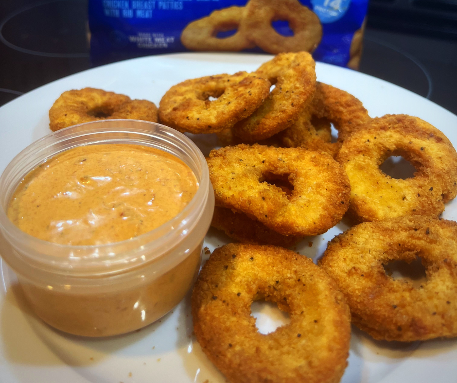 Plate with a cup of orange sauce and circular chicken nugget rings