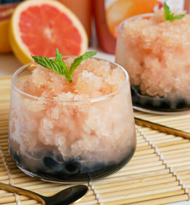 close up of clear glass on top of a bamboo mat filled filled with blended ice on top of tapioca balls