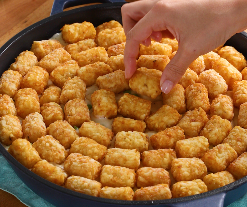 a layer of tater tots in a skillet with a hand reaching in to grab one