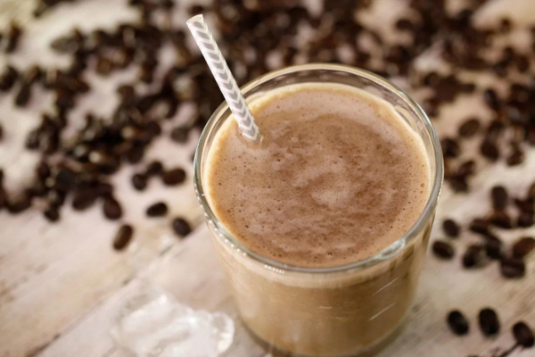 An overhead shot of a glass filled with a java cream smoothie with a straw and out of focus coffee beans in the background 