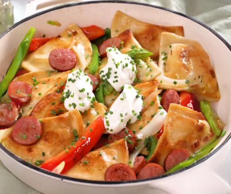 Pierogies, kielbasa, sour cream, and sauteed vegetables in a skillet