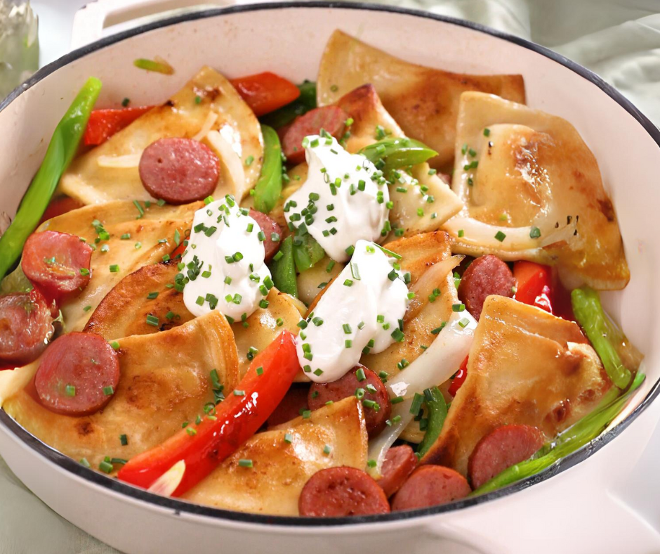 Pierogies, kielbasa, sour cream, and sauteed vegetables in a skillet