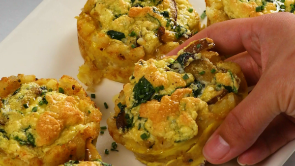 hand lifting a spinach and egg cup off of a plate