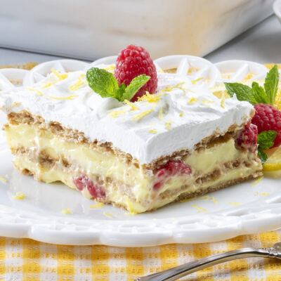 Close up shot of lemon raspberry ice box cake on top of a white plate with a yellow gingham print table cloth underneath and a fork