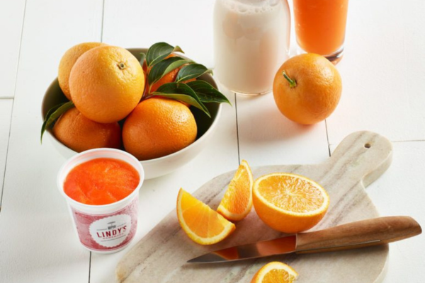 Bowl of oranges with Orange Lindy's Italian Ice in front of it and a cutting board with sliced oranges to the right