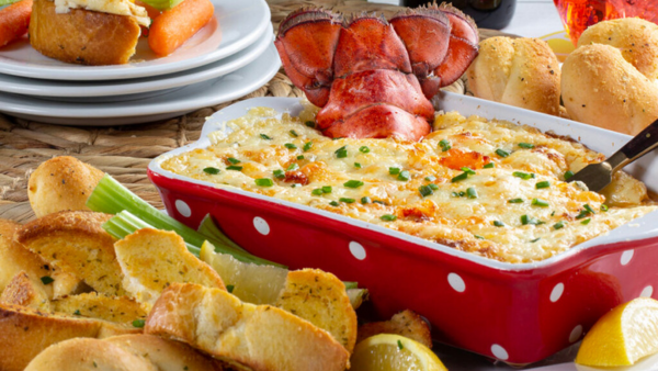 a casserole dish filled with lobster roll dip sitting next to a few pieces of garlic bread