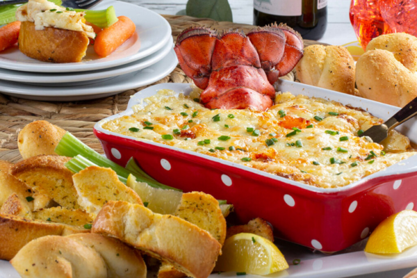 a casserole dish filled with lobster roll dip sitting next to a few pieces of garlic bread