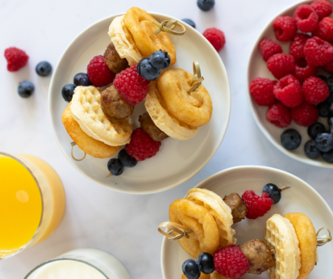 Two plates with mini breakfast skewers on top next to a bowl of berries
