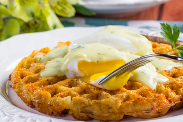 Hash brown waffle with a runny egg on top and a fork dipping into the egg