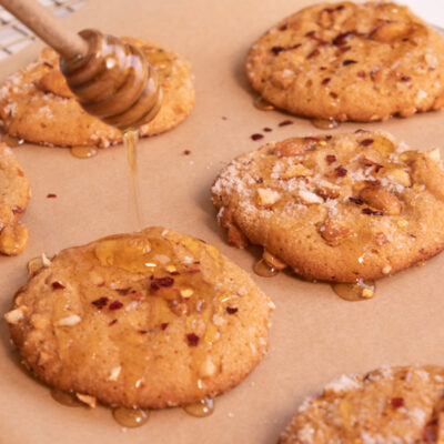 Close up image of 4 hot honey peanut butter cookies with hot honey being drizzled from a honeycomb