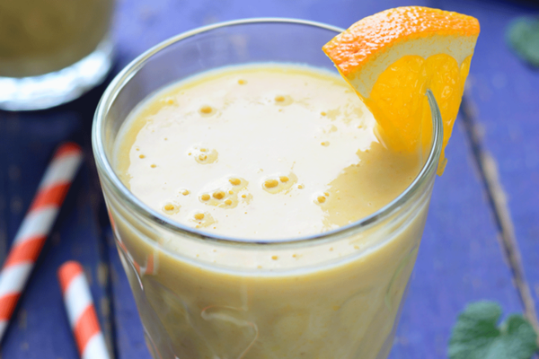 close up of a glass filled with an orange smoothie with an orange slice on the rim