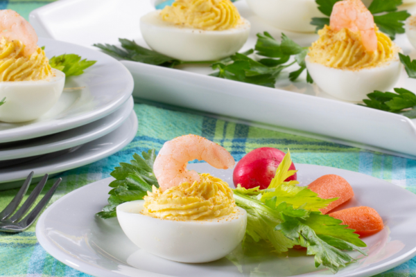 Close up image of a deviled egg with shrimp on top on a plate