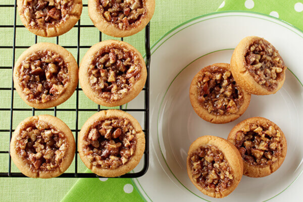 Pecan pie bites on a baking tray next to a plate of pecan pie bites