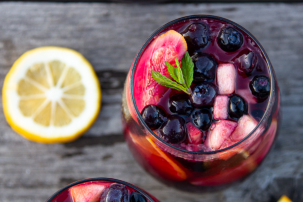 Overview image of a glass of pomegranate-blueberry sangria mocktail with a lemon slice to the left