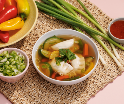 a bowl of potsticker veggie soup, a small bowl of chopped green onions, and raw green onions all sitting on a woven table mat