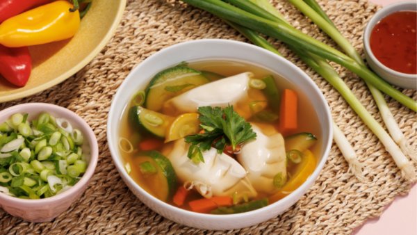a bowl of potsticker veggie soup, a small bowl of chopped green onions, and raw green onions all sitting on a woven table mat