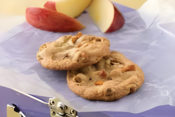 two pretzel chip cookies stacked on one another with apple slices in the background