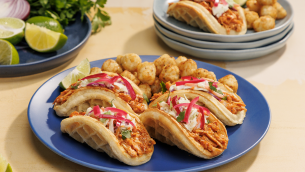 Four pulled chicken waffle tacos and tater tots on a blue plate