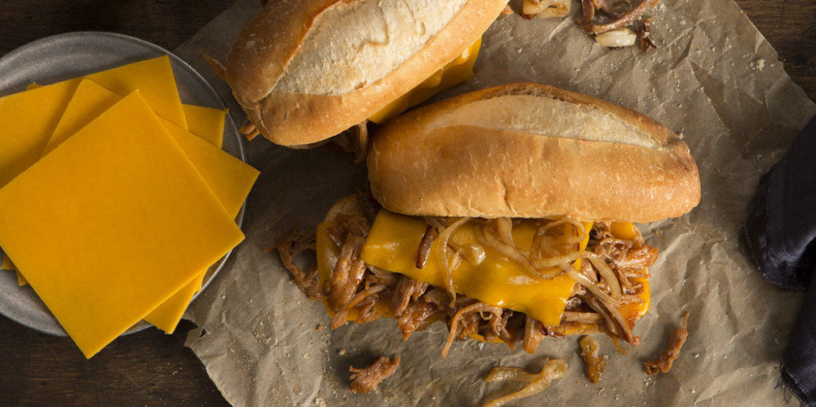 Pulled pork sandwich laying next to a pile of sliced cheese
